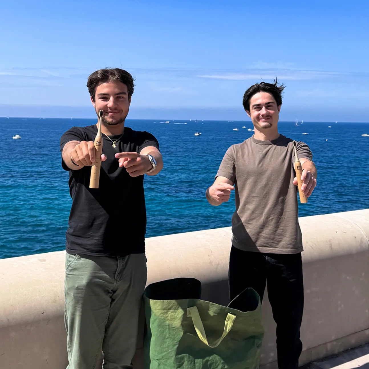 Deux utilisateurs tenant une brosse à dents électrique en bambou Pulse Care en extérieur face à la mer