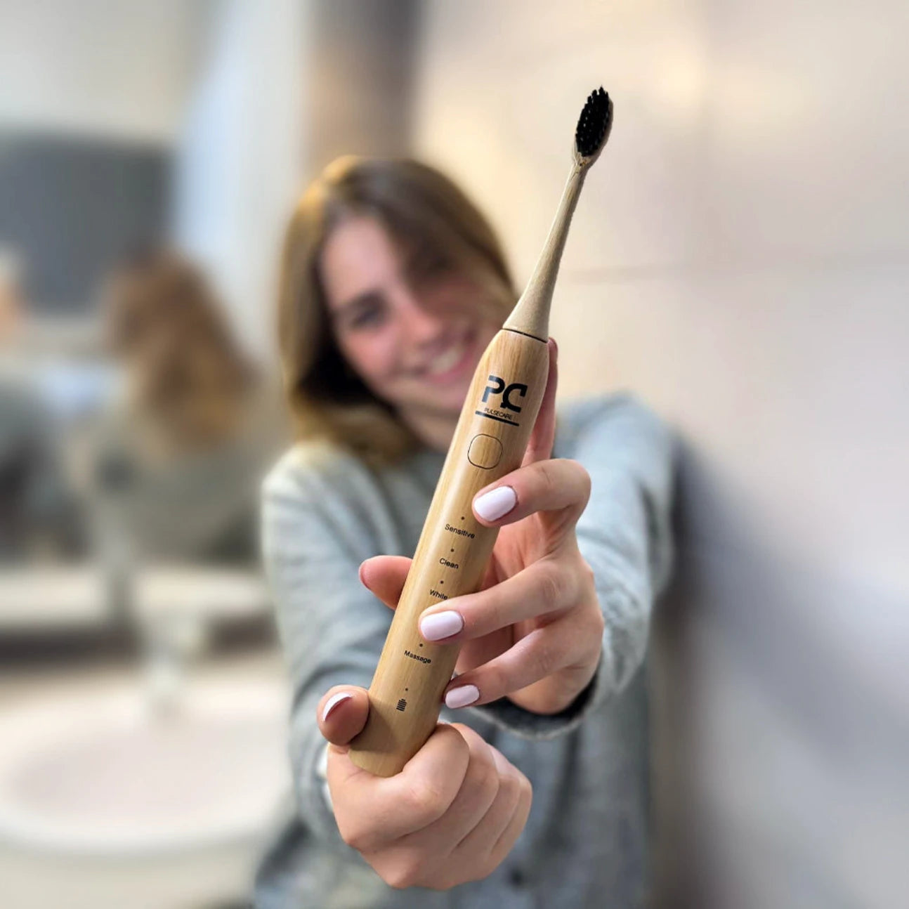Femme tenant une brosse à dents électrique en bambou Pulse Care dans une salle de bain